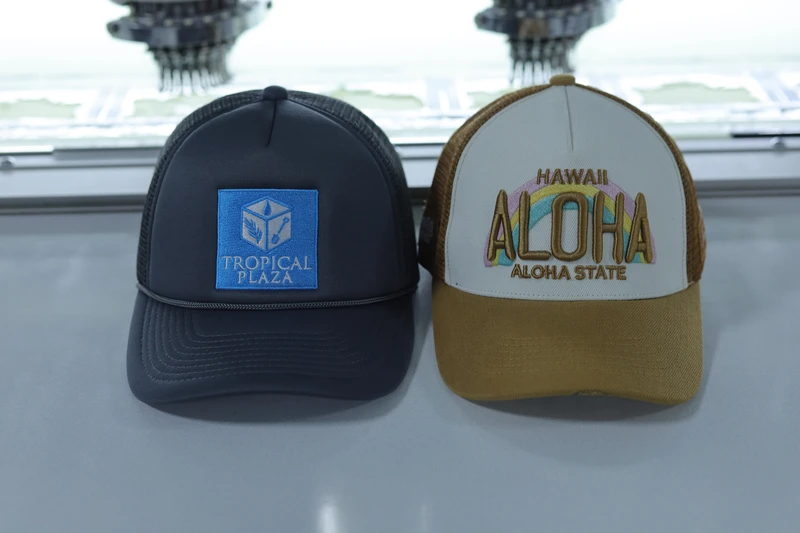 Two custom trucker cap samples with embroidered front designs, photographed by embroidery machines