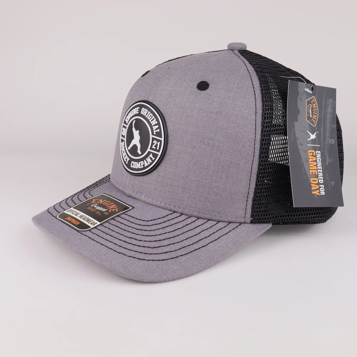 Grey patch trucker cap with black mesh and attached sample tags, three-quarter view