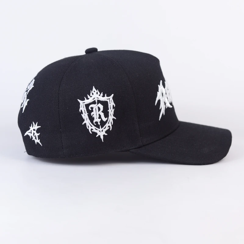 Side of black structured cap showing ornate white crest-style embroidery on crown panel