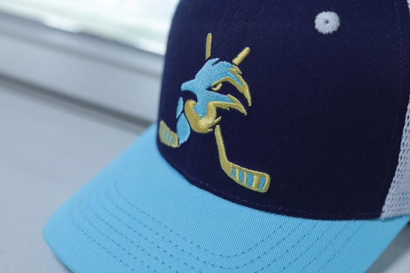 Close view of yellow and aqua mascot embroidery on the navy trucker front above the aqua visor