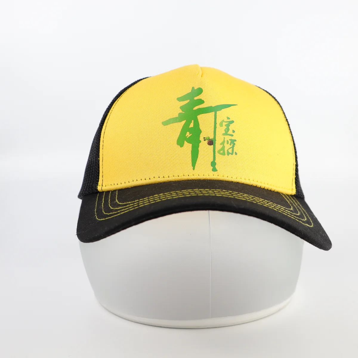 Yellow-front trucker cap with green artwork, black visor and contrast visor stitching